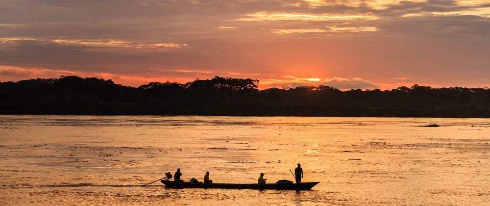 Vue d'une pirogue naviguant en Amazonie dans la lumière rose du soleil couchant.