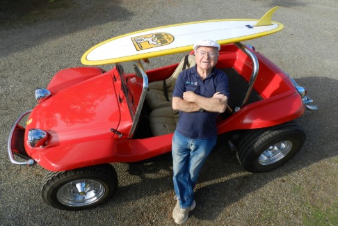 l'inventeur du buggy adossé à un buggy rouge avec une planche de surf sur le toit.