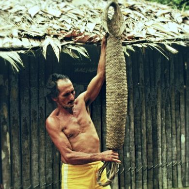 Caboclo montrant un panier a presser le manioc indigène devant sa cabane en Amazonie.