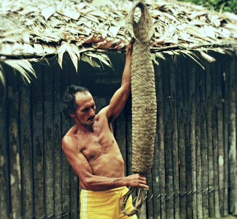 Caboclo montrant un panier a presser le manioc indigène devant sa cabane en Amazonie.