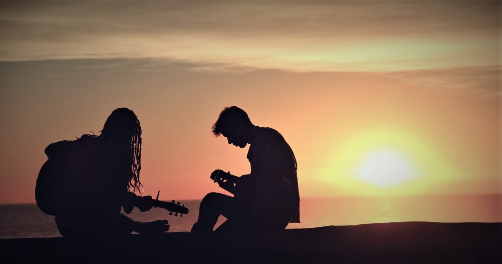 2 personne jouant de la guitare a contre jour dans le soleil couchant sur la plage.