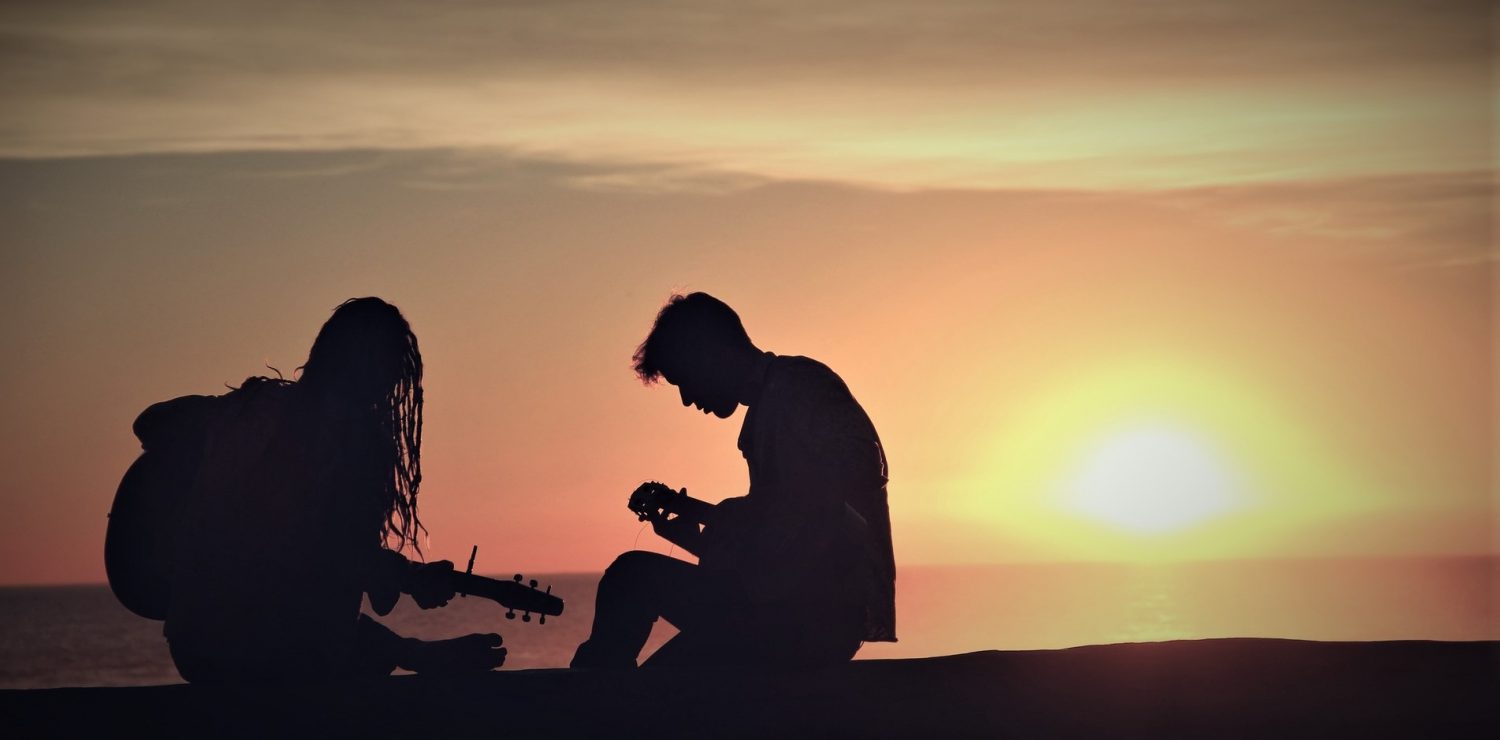 2 personne jouant de la guitare a contre jour dans le soleil couchant sur la plage.