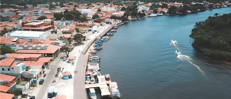 Vue aérienne de Barreirinhas au Maranhão avec le fleuve Preguiças, ses bateaux amarrés le long des quais et deux vedettes naviguant sur l'eau.