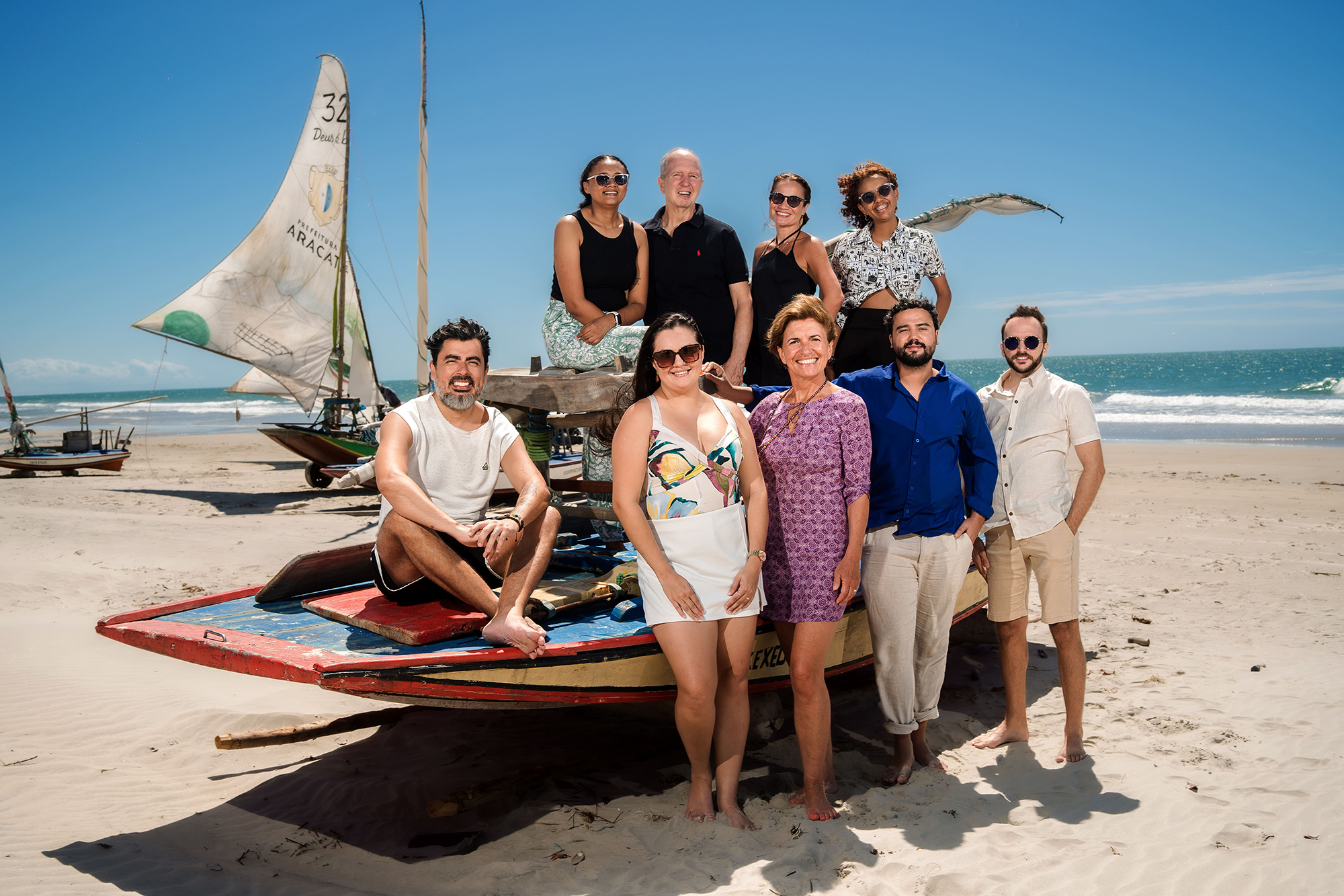 Photo de groupe des neuf membres de l'équipe de Brazil Selection, souriants en tenue d'été autour d'une embarcation traditionnelle en bois sur la plage de Fortim, sous un ciel bleu azur.