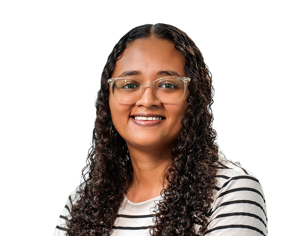 Portrait de Bruna, chargée de production et expertise terrain pour l'agence Brazil Selection, souriante, portant des lunettes et un haut rayé noir et blanc sur fond blanc uni.