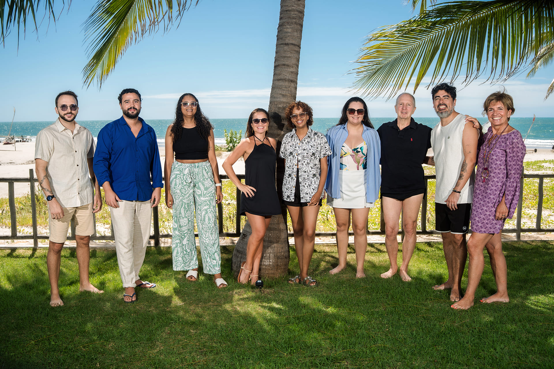 Les neuf membres de l'équipe Brazil Selection alignés et souriants sur de la pelouse devant un cocotier, avec la plage et la mer en arrière-plan par beau temps.
